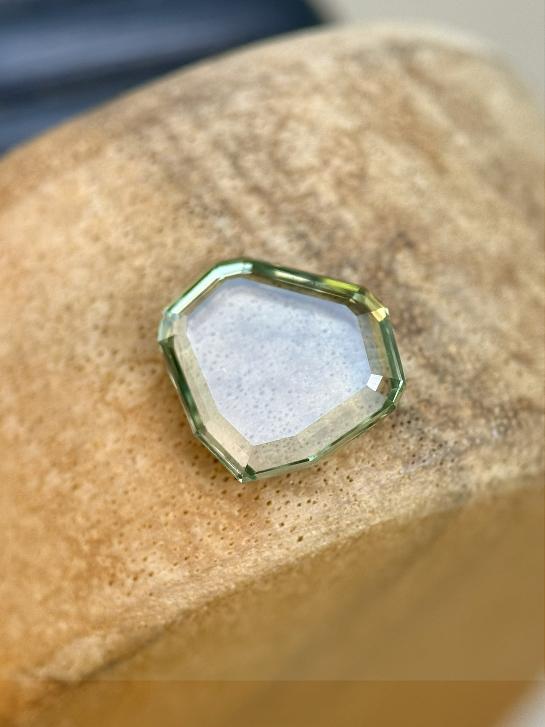 Custom shield portrait cut Montana sapphire in bluish seafoam green, weighing 2.58 carats, shown at an angle on a stone surface
