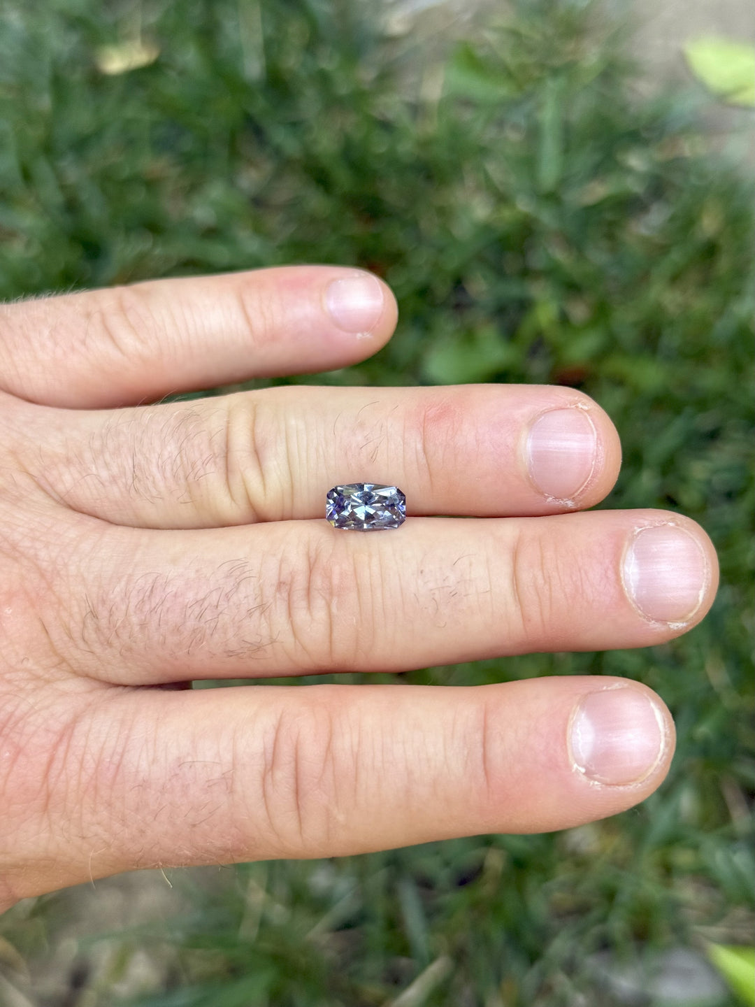 1.84ct Tanzanite resting on fingers, showing natural unheated color play of green, lavender, and purple in daylight.