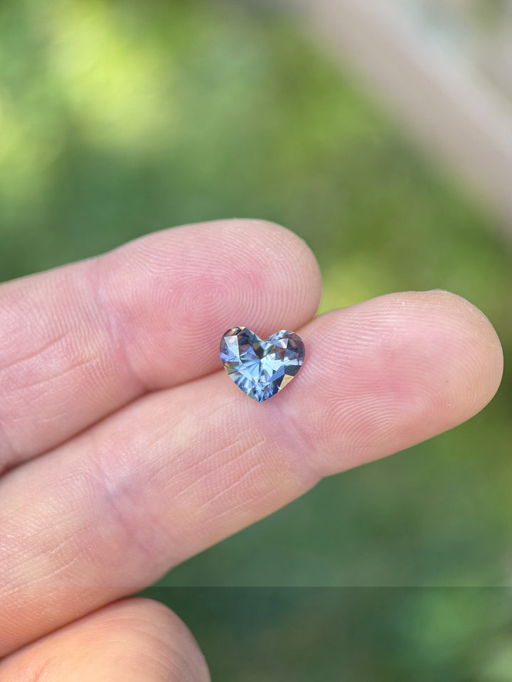 Natural untreated Tanzanite gemstone in heart shape showing vibrant blues and purples on fingertips