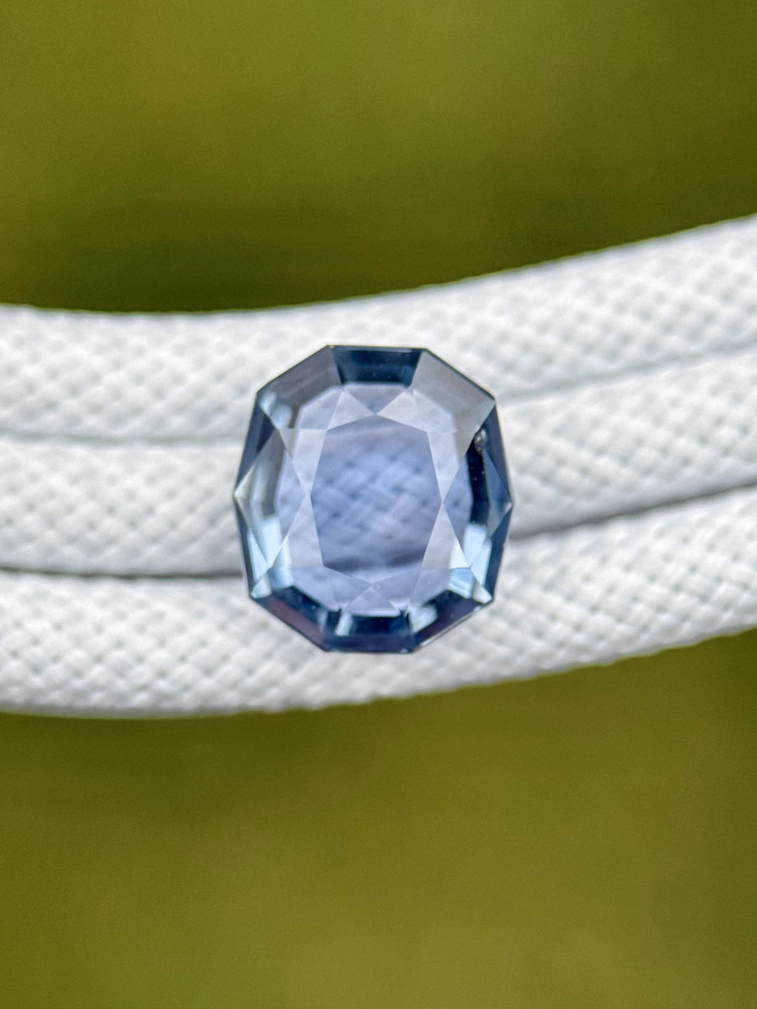 Blue and violet Montana sapphire placed on textured white rope, highlighting its clean cushion tablet cut and natural brilliance.