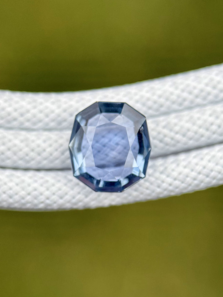 Blue and violet Montana sapphire placed on textured white rope, highlighting its clean cushion tablet cut and natural brilliance.