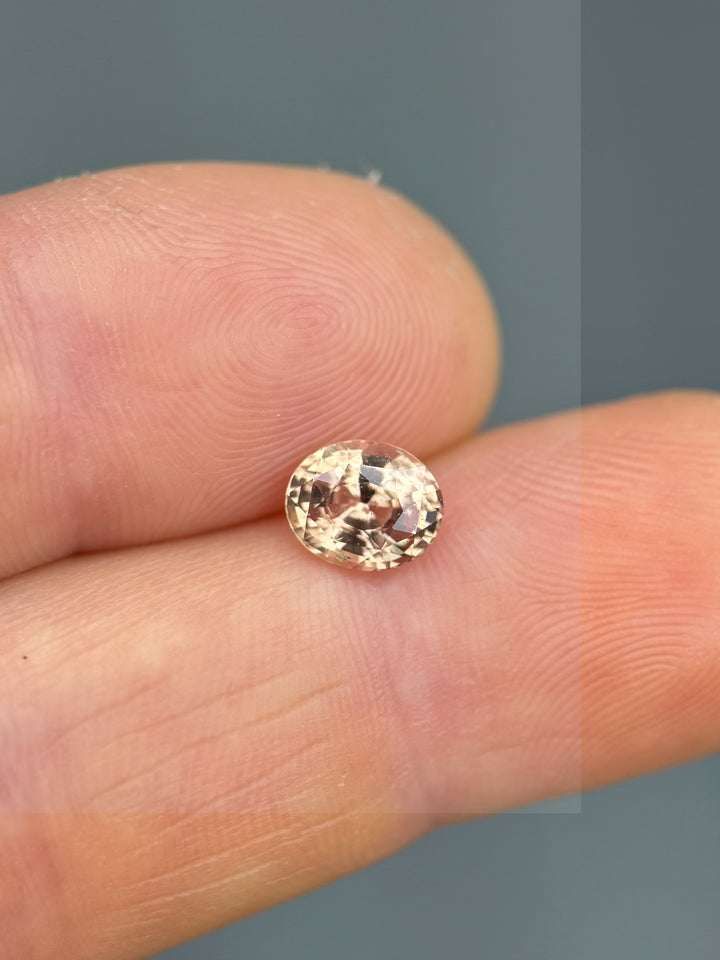 Unheated 1.51-carat oval sapphire with peachy-pink tones, shown on fingertip for scale and clarity