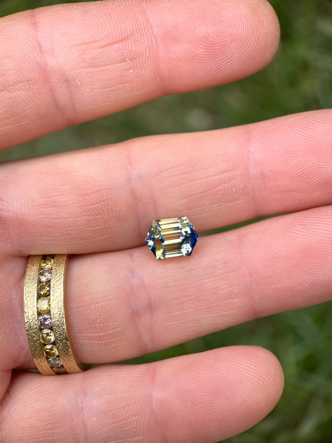Top-down view of a bi-color sapphire held in hand, revealing clean step faceting and crisp blue-yellow color zoning.