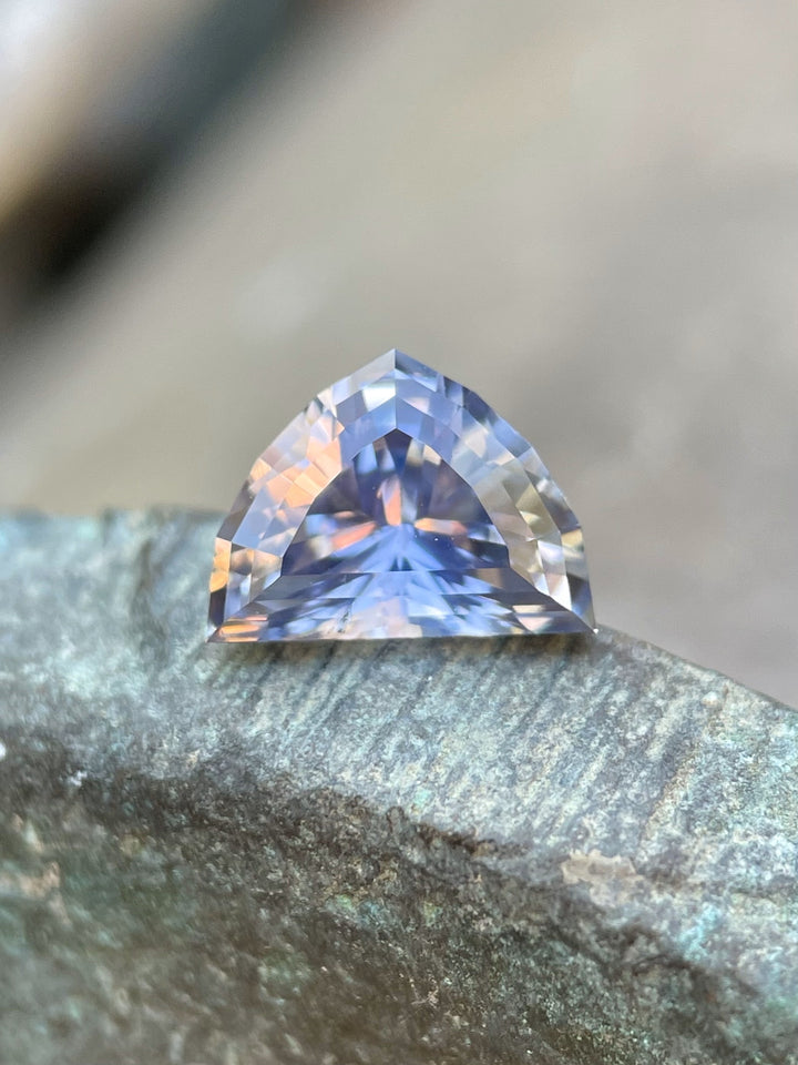Close-up of a 1.66-carat sapphire resting on a textured surface, revealing its stunning periwinkle and lavender hues.