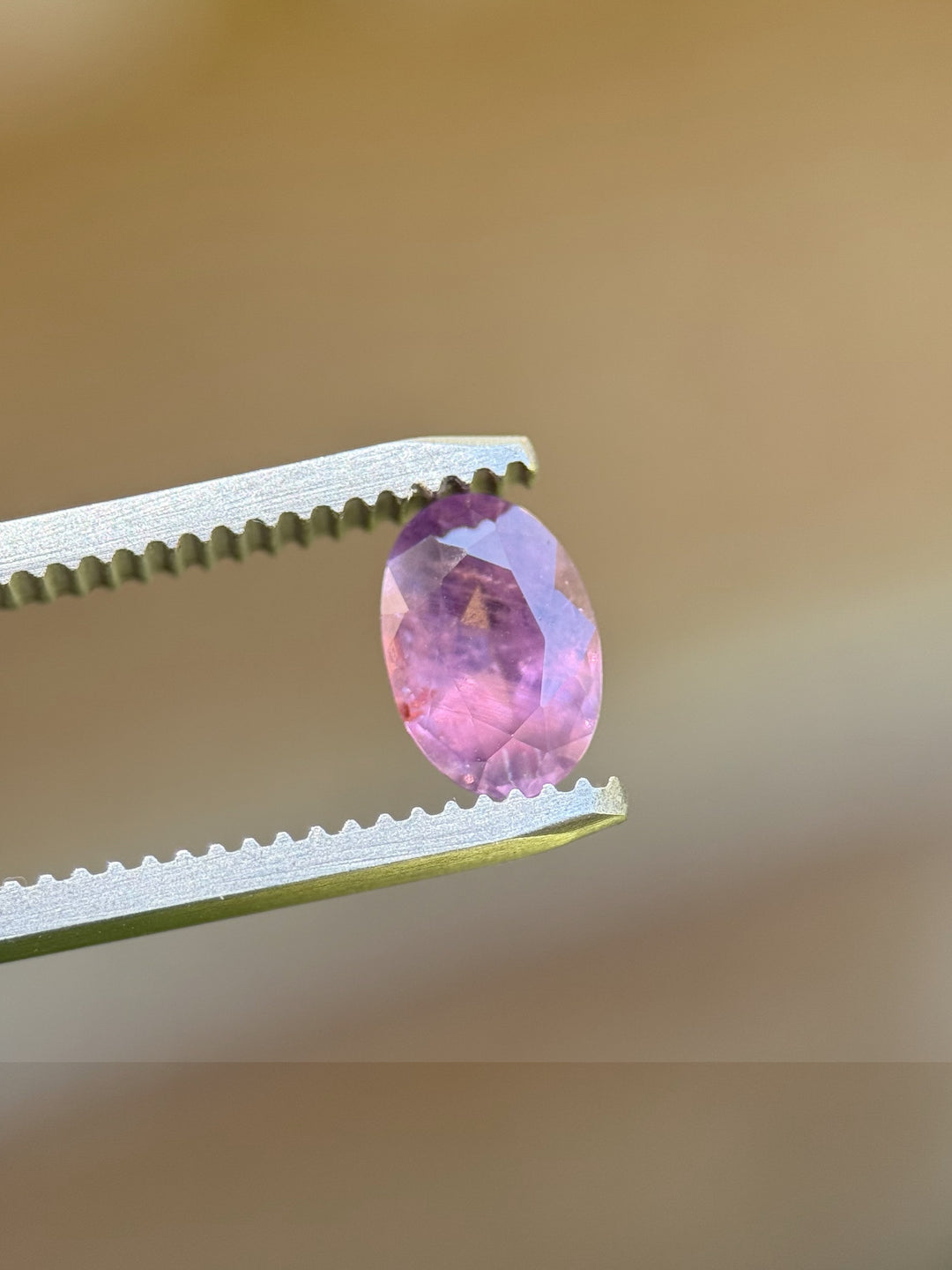 Unheated 1.37ct Umba sapphire held in tweezers with pink-purple hues visible through clean oval facets.