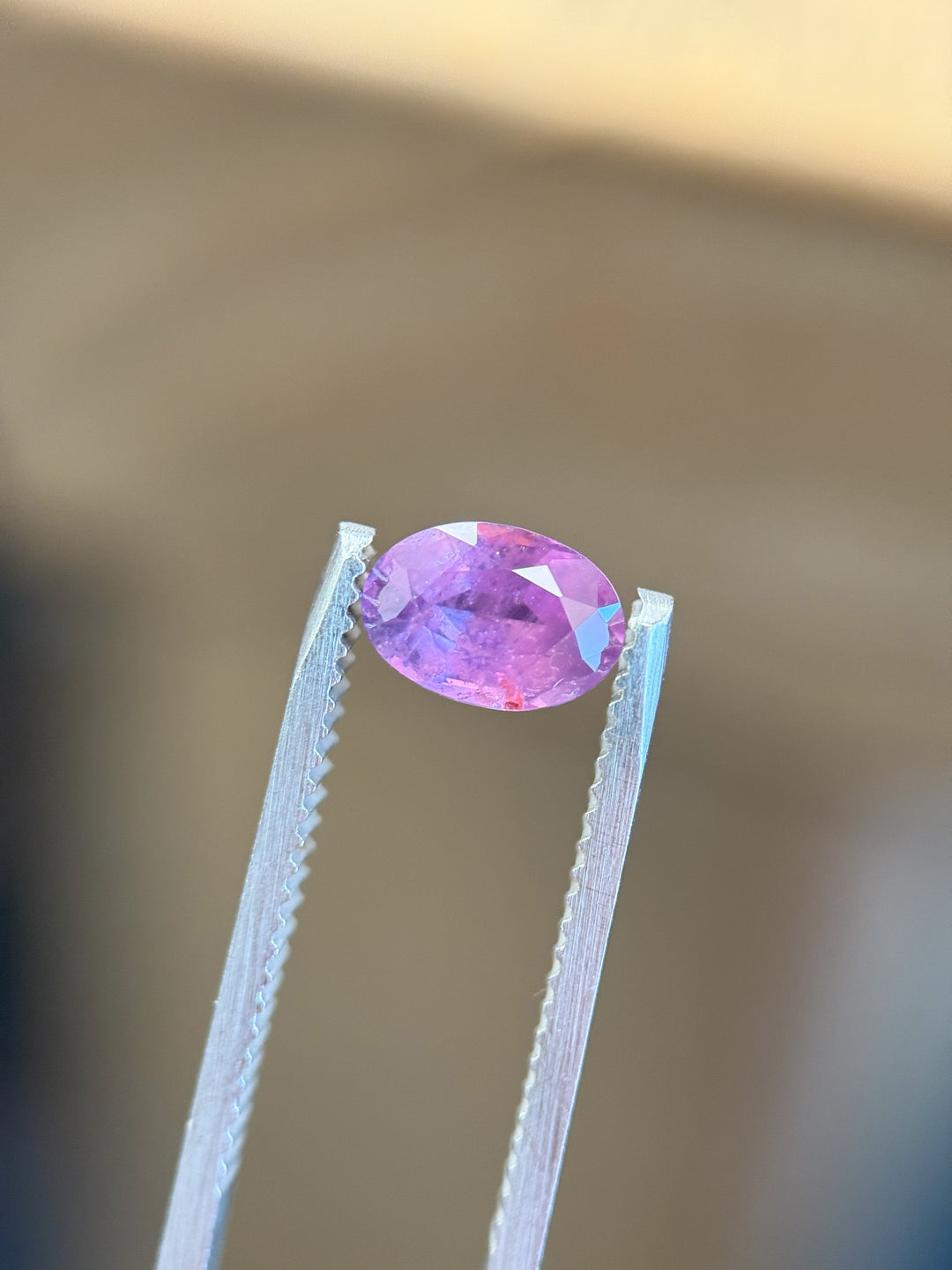 Custom oval-cut Umba River sapphire showcasing a vibrant pink and purple mix in studio lighting.