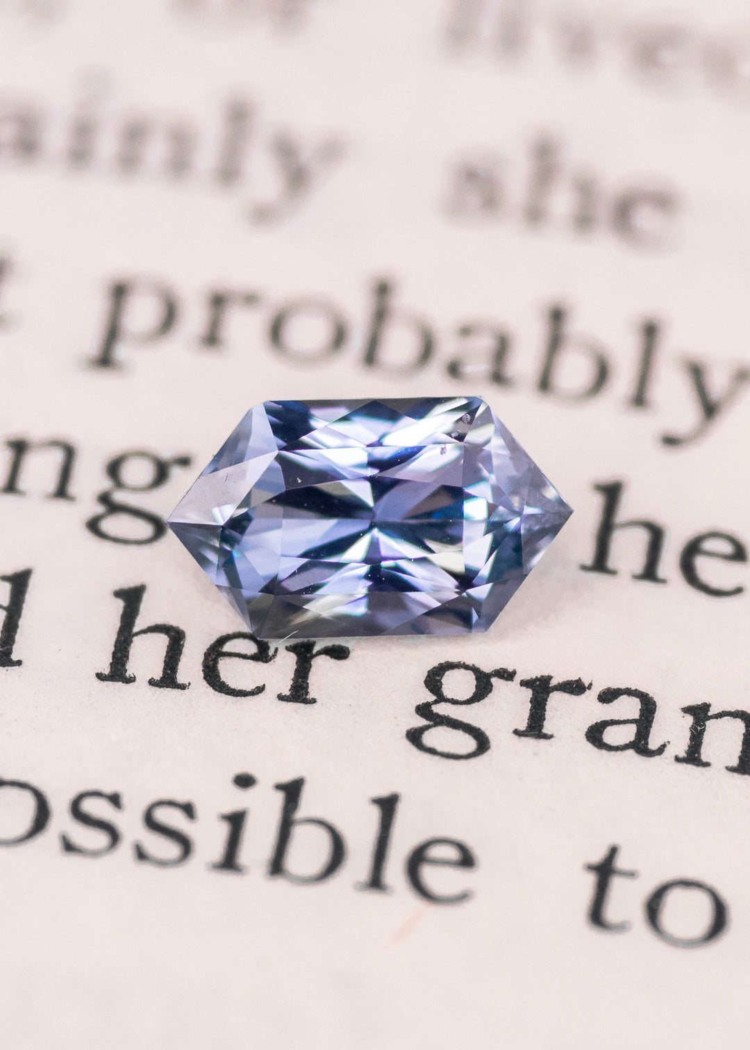 Elongated hexagon seafoam grey blue sapphire photographed on printed book text, showcasing mirror-like facets, cool blue-gray color, and precision mixed cut, 1.11 carat unheated sapphire from Sakaraha Madagascar