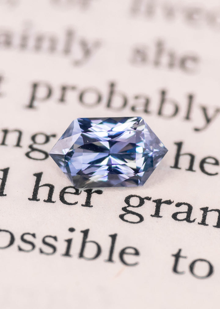 Elongated hexagon seafoam grey blue sapphire photographed on printed book text, showcasing mirror-like facets, cool blue-gray color, and precision mixed cut, 1.11 carat unheated sapphire from Sakaraha Madagascar