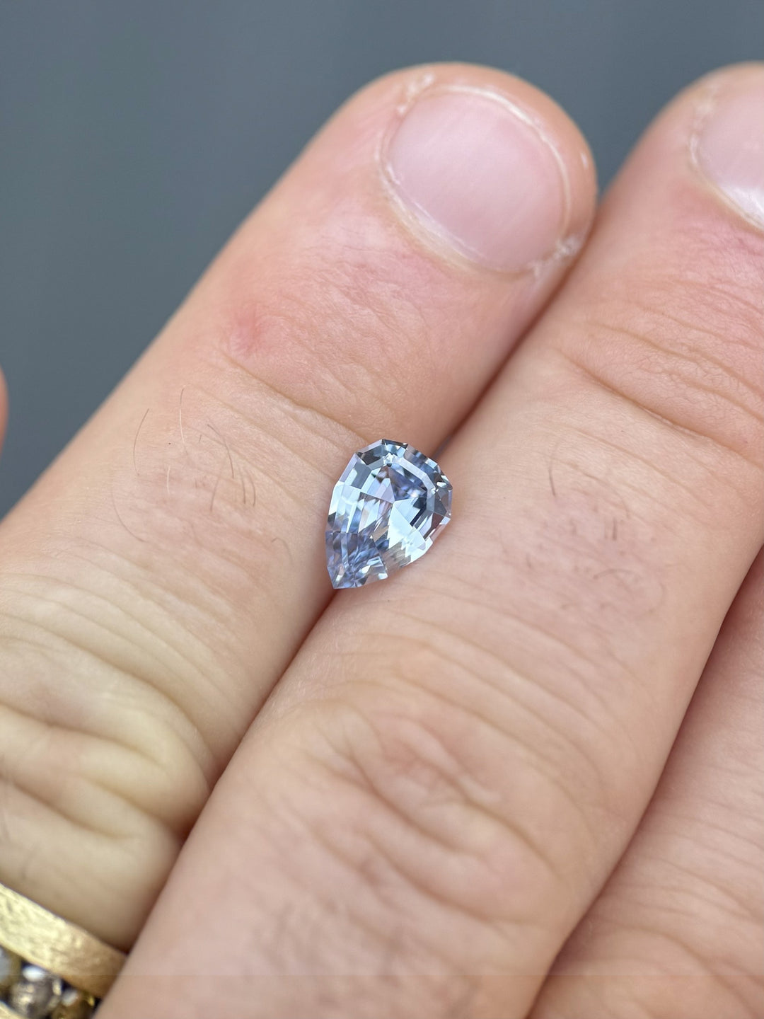 1.67ct Sri Lankan sapphire in soft powder blue displayed on a finger to show scale, geometric pear brilliant cut