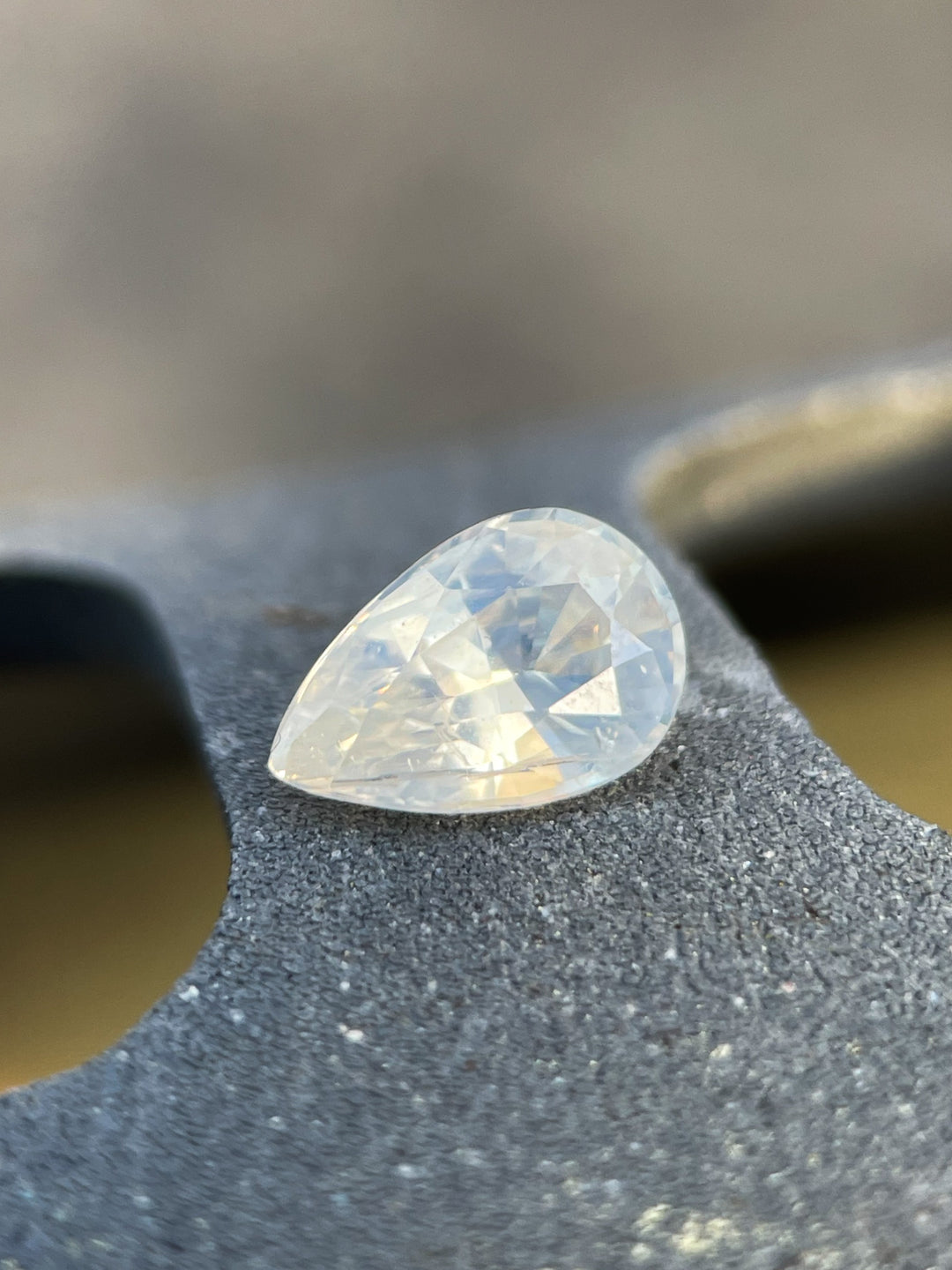 Custom shield-cut pale yellow sapphire resting on a textured surface, highlighting its faceted precision and luminous clarity.