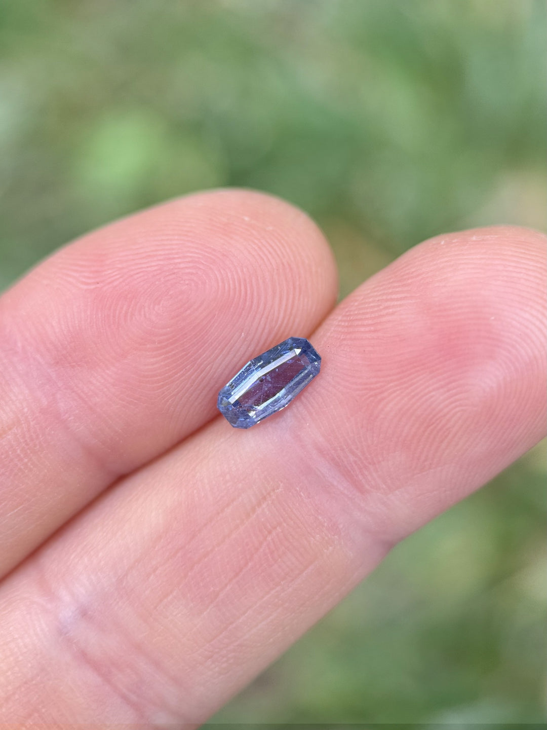 1.05 carat unheated cornflower blue sapphire displayed on fingertip outdoors – Umba River origin, elongated cushion step cut