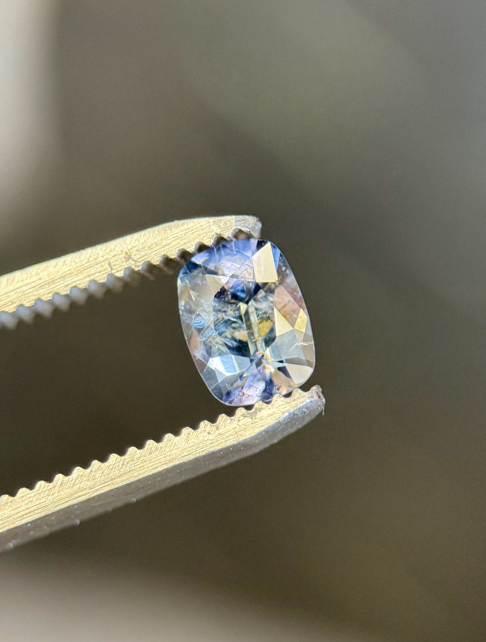 Close-up of a 1.23-carat teal to purple color-shifting sapphire in antique cushion cut, held with gem tweezers.
