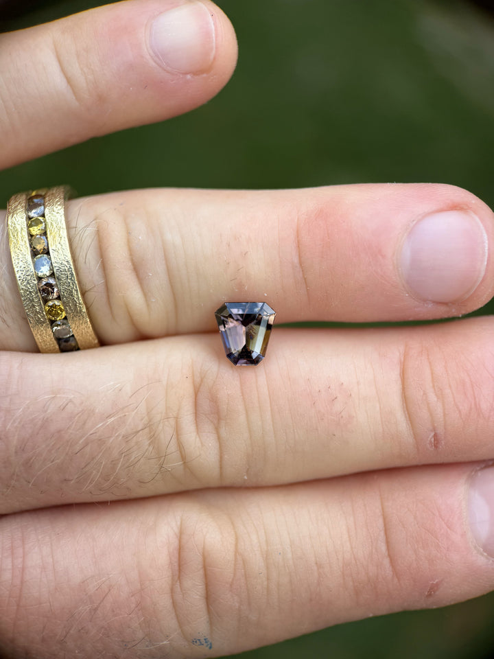 1.68 carat Tanzanite with green, yellow, and purple tones shown resting on fingertips for scale.
