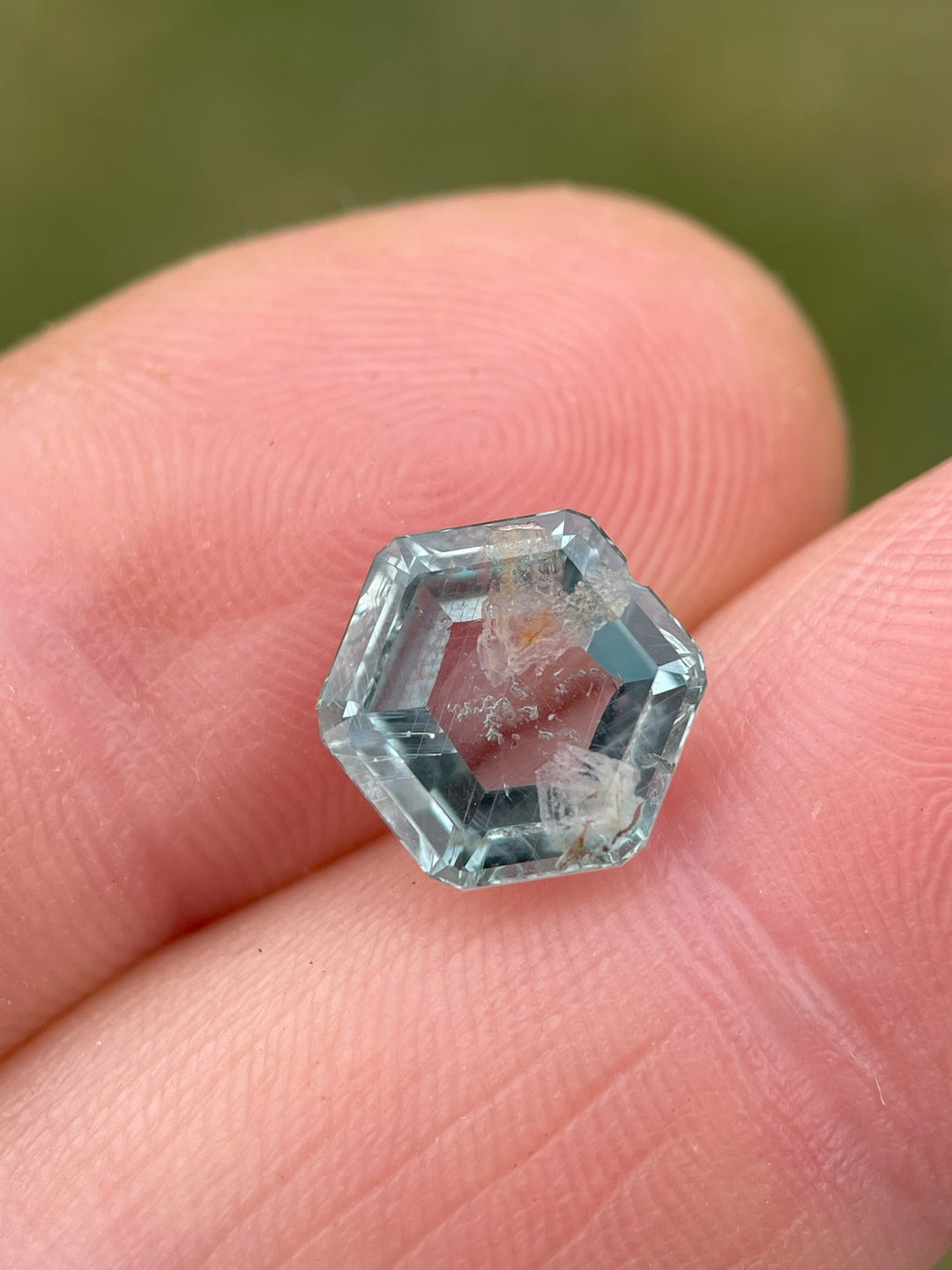 Hexagon-shaped teal green sapphire weighing 4.00 carats, showcased in a close-up image on fingertips.