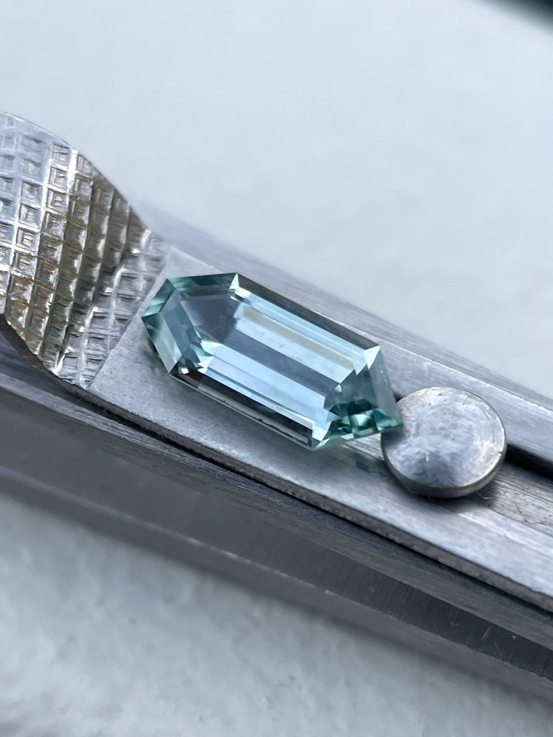 Close-up of a 1.05 carat Montana sapphire with a unique septagon bullet cut in blue and teal hues, resting on a jeweler's tool.