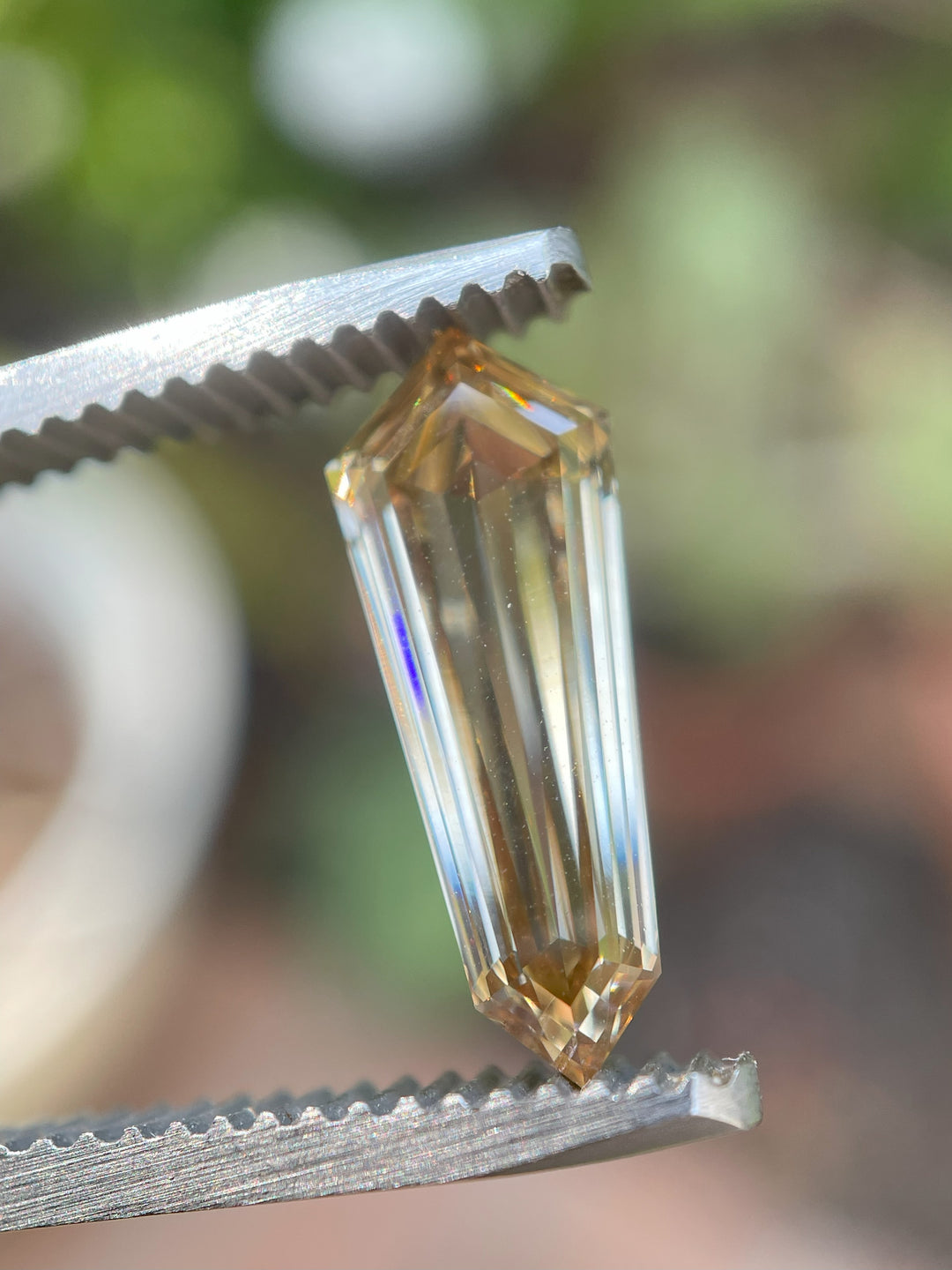 Macro shot of a 2.02-carat VVS2 clarity champagne diamond in tweezers, reflecting golden brown tones under natural light.