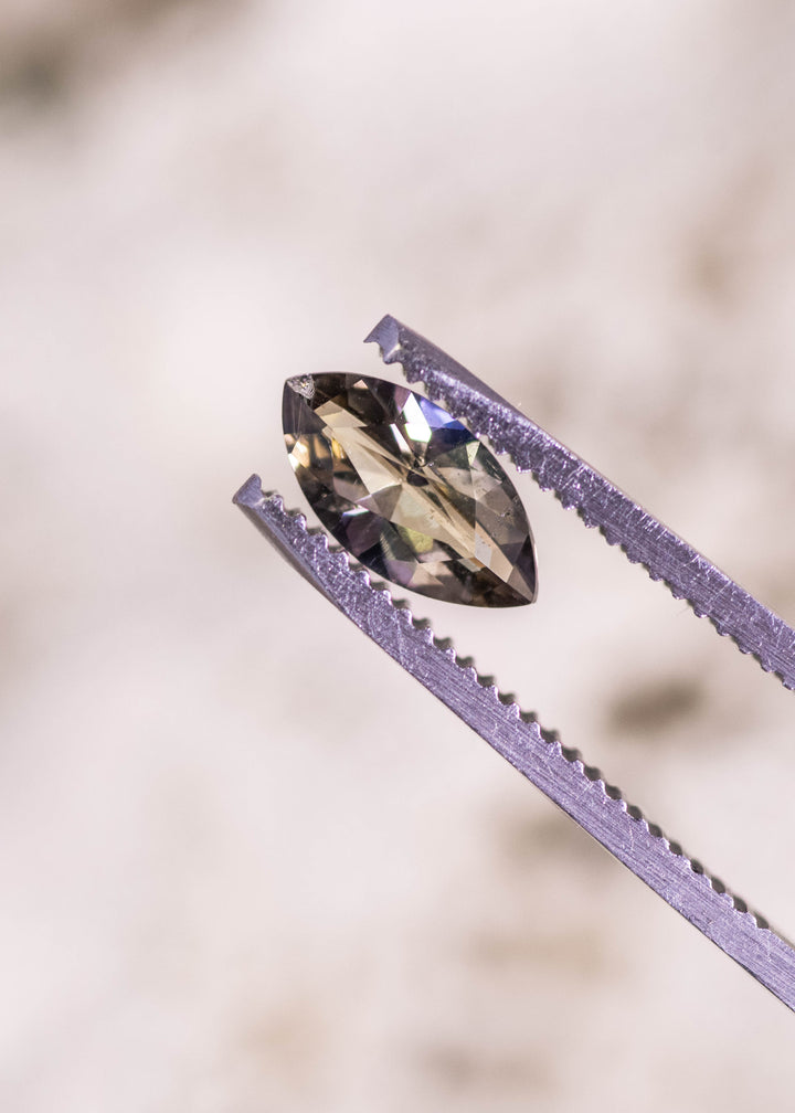 Marquise brilliant cut tanzanite held in gem tweezers, displaying yellow, teal, and green color tones, sharp facet symmetry, and untreated clarity from Merelani Hills, Tanzania