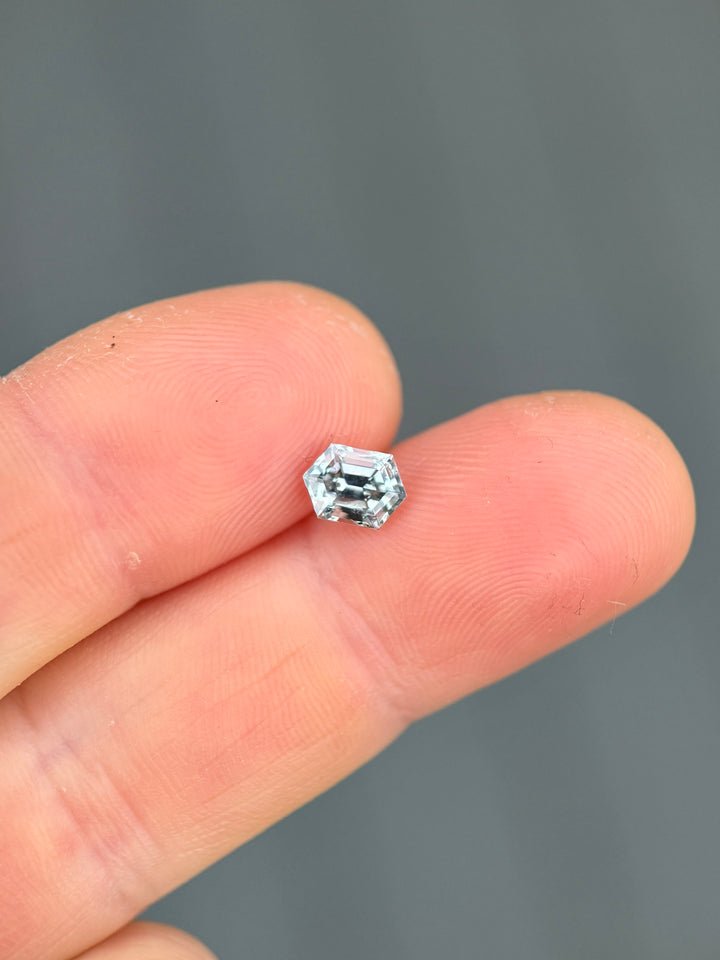 1.22CT Montana sapphire balanced on fingertip for scale, highlighting elongated hexagon step cut geometry, crisp facet structure, and subtle seafoam to grey silver color shift in natural daylight.