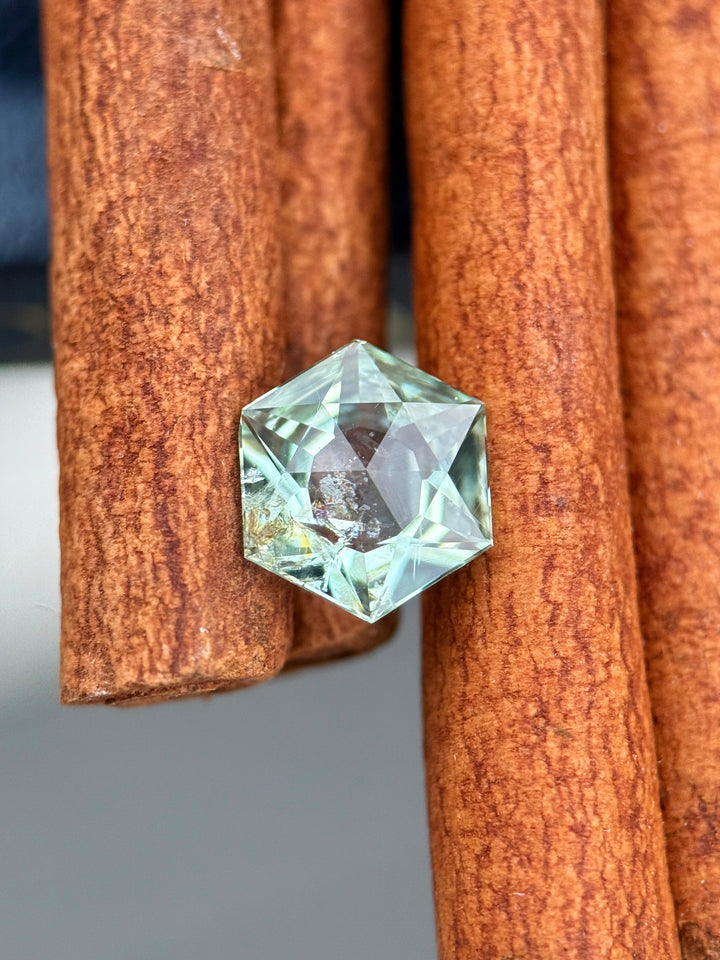Mint sage teal green Montana sapphire photographed on natural cinnamon sticks, highlighting the precision hexagon mixed cut, open culet, and crisp facet reflections of this 1.76 carat untreated sapphire