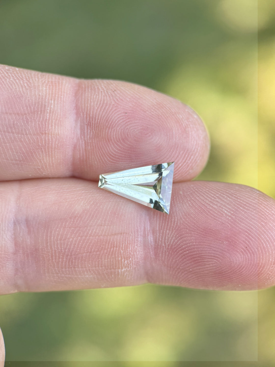Mint green tourmaline weighing 2.02 carats shown on fingertip for scale, highlighting its elongated tapered baguette step cut and natural brilliance, untreated gemstone from Congo, Africa.