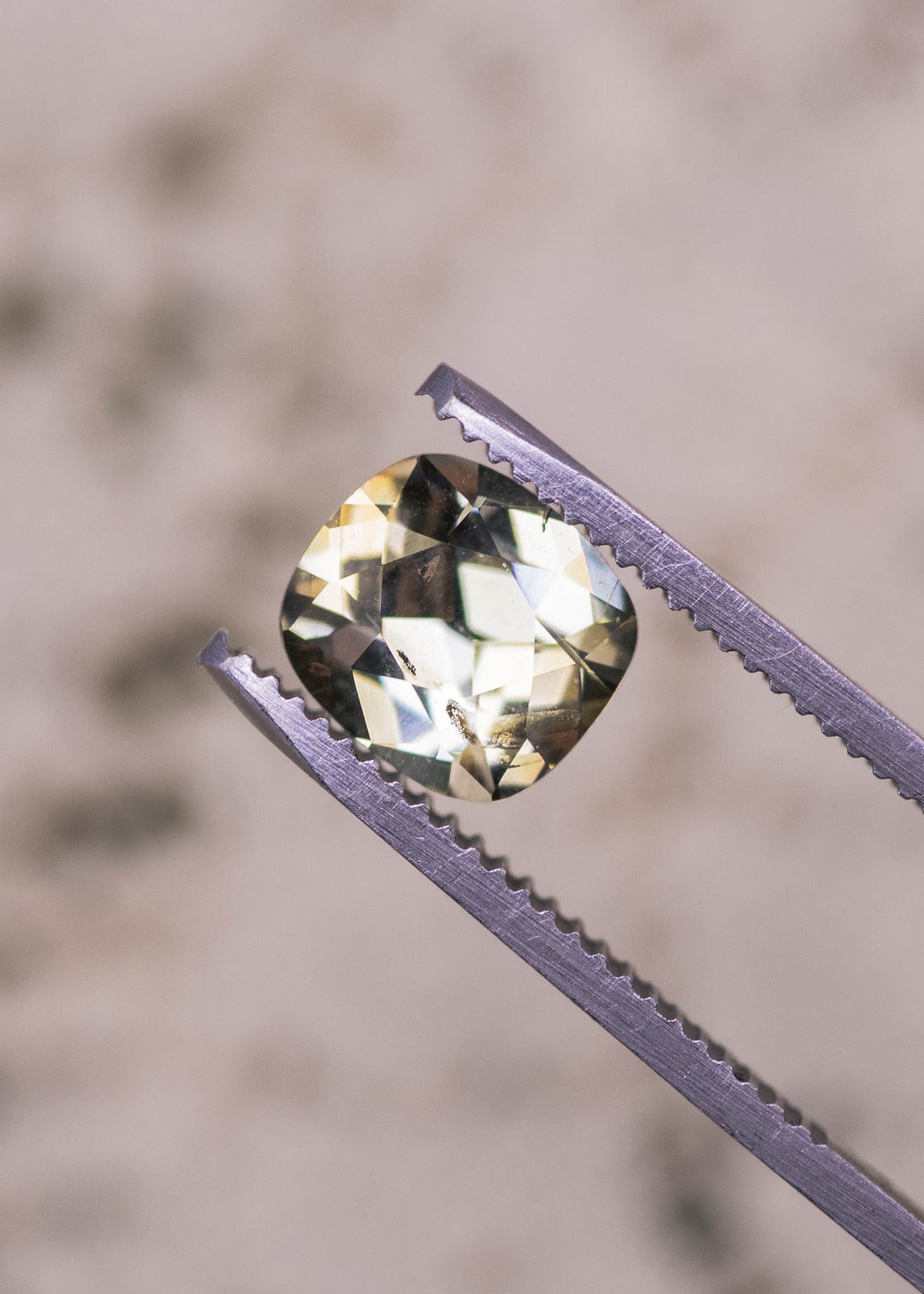 Cushion brilliant cut yellow green Tanzanite held in gem tweezers, highlighting pavilion depth, facet symmetry, and natural untreated clarity from Merelani Hills, Tanzania