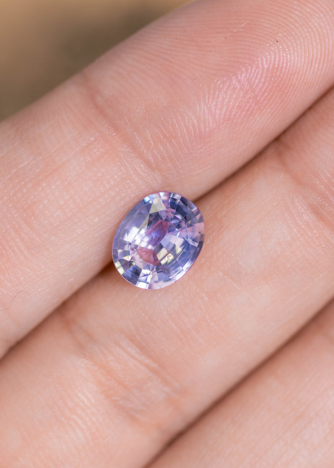 2.25 carat gray pink sapphire displayed on fingertip for scale, natural oval mix cut sapphire from Sri Lanka with subtle pink and clear zoning