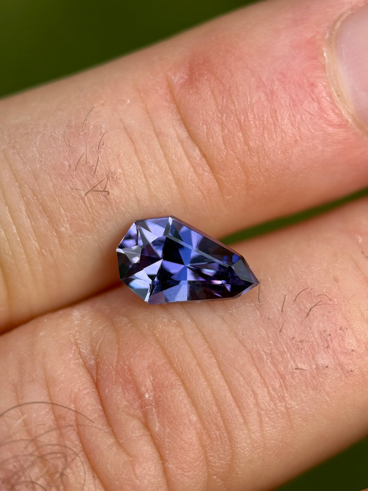 2.47 carat Tanzanite resting on fingertips, showing the depth of its slightly greenish blue and purple tones under natural daylight, cut in a custom shield mixed cut and sourced ethically from Merelani Hills, Tanzania.