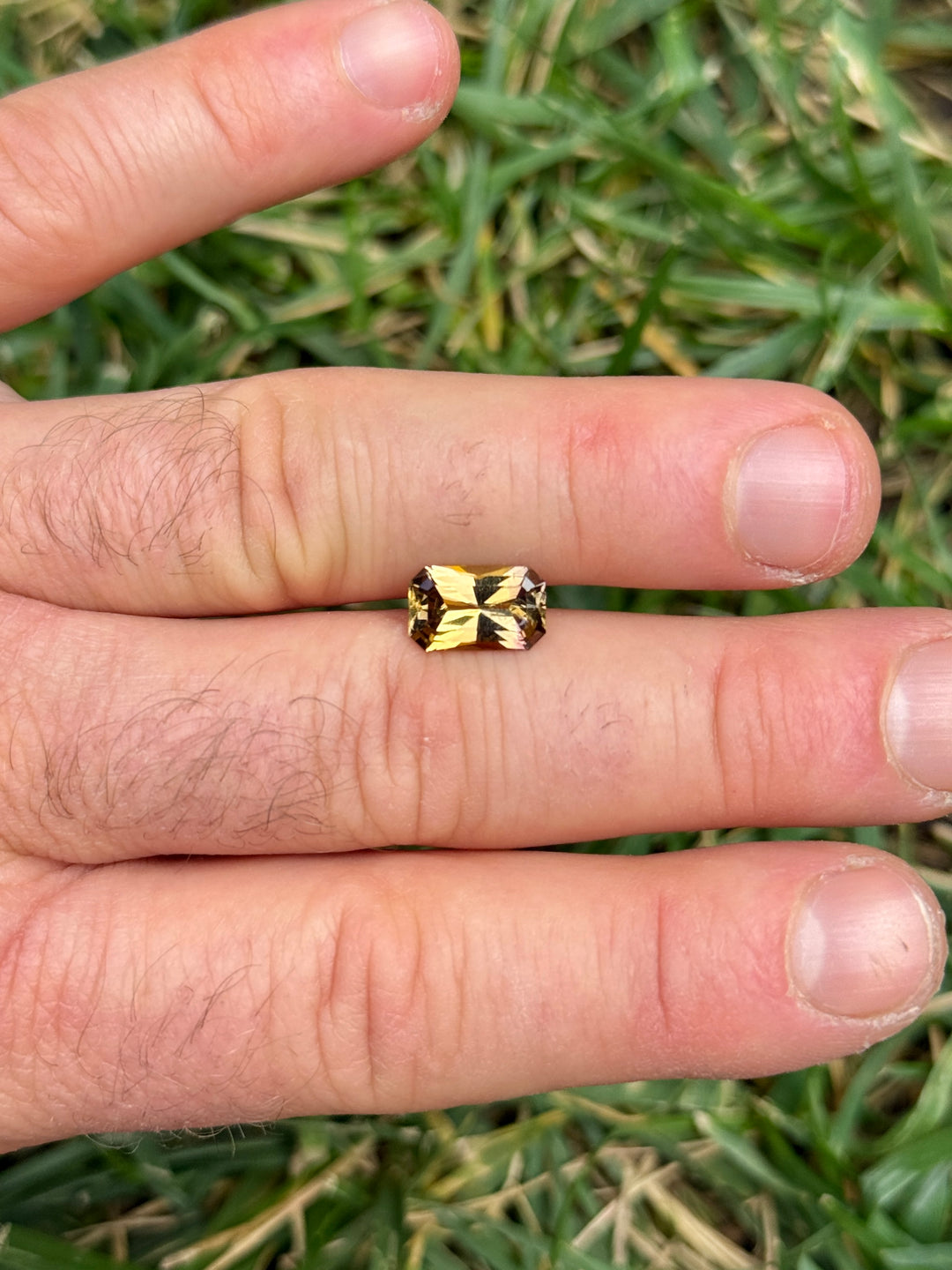 2.63 carat Tanzanite placed on fingers for size comparison, revealing vivid golden and purple hues with radiant sparkle, custom octagon radiant cut, untreated and natural gem from Merelani Hills, Tanzania.