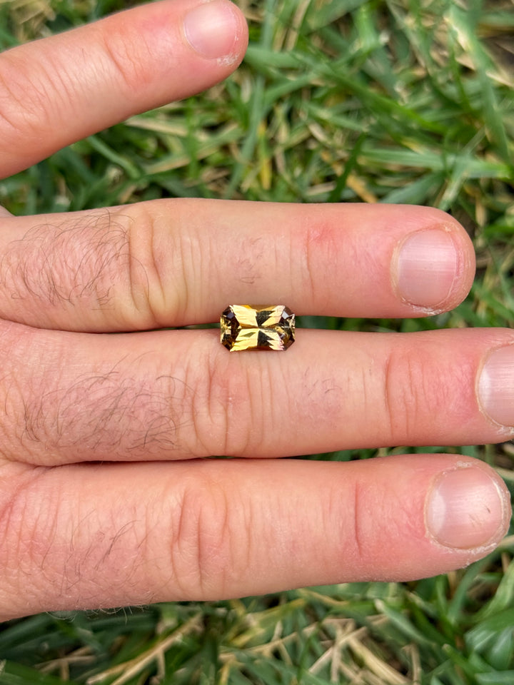 2.63 carat Tanzanite placed on fingers for size comparison, revealing vivid golden and purple hues with radiant sparkle, custom octagon radiant cut, untreated and natural gem from Merelani Hills, Tanzania.
