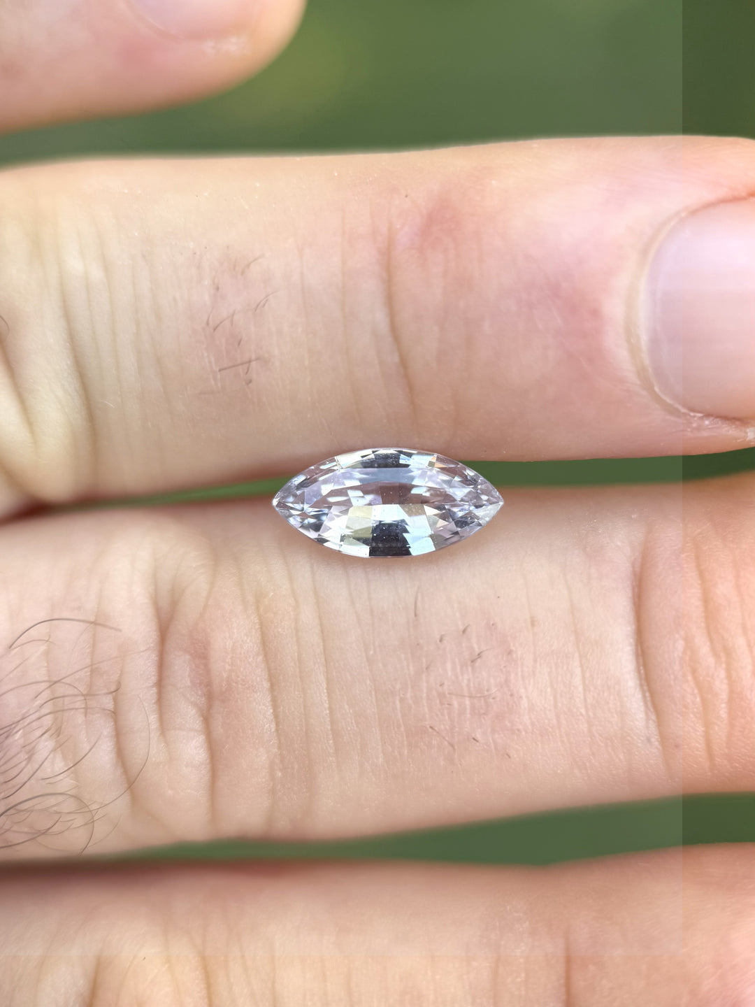 Light silvery lilac 2.68 carat sapphire resting on fingertip for size reference, showing marquise mixed cut sparkle and natural brilliance, untreated gemstone from Sakaraha, Madagascar.