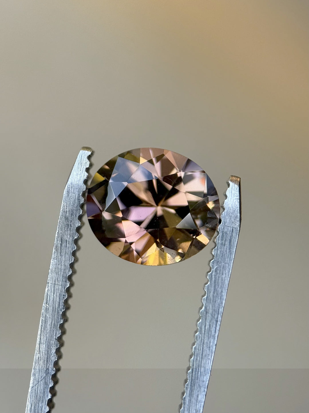 Close-up of 2.76ct roval brilliant Tanzanite held in tweezers, showing untreated Merelani Hills gem’s vivid color play of peach, pink, and purple