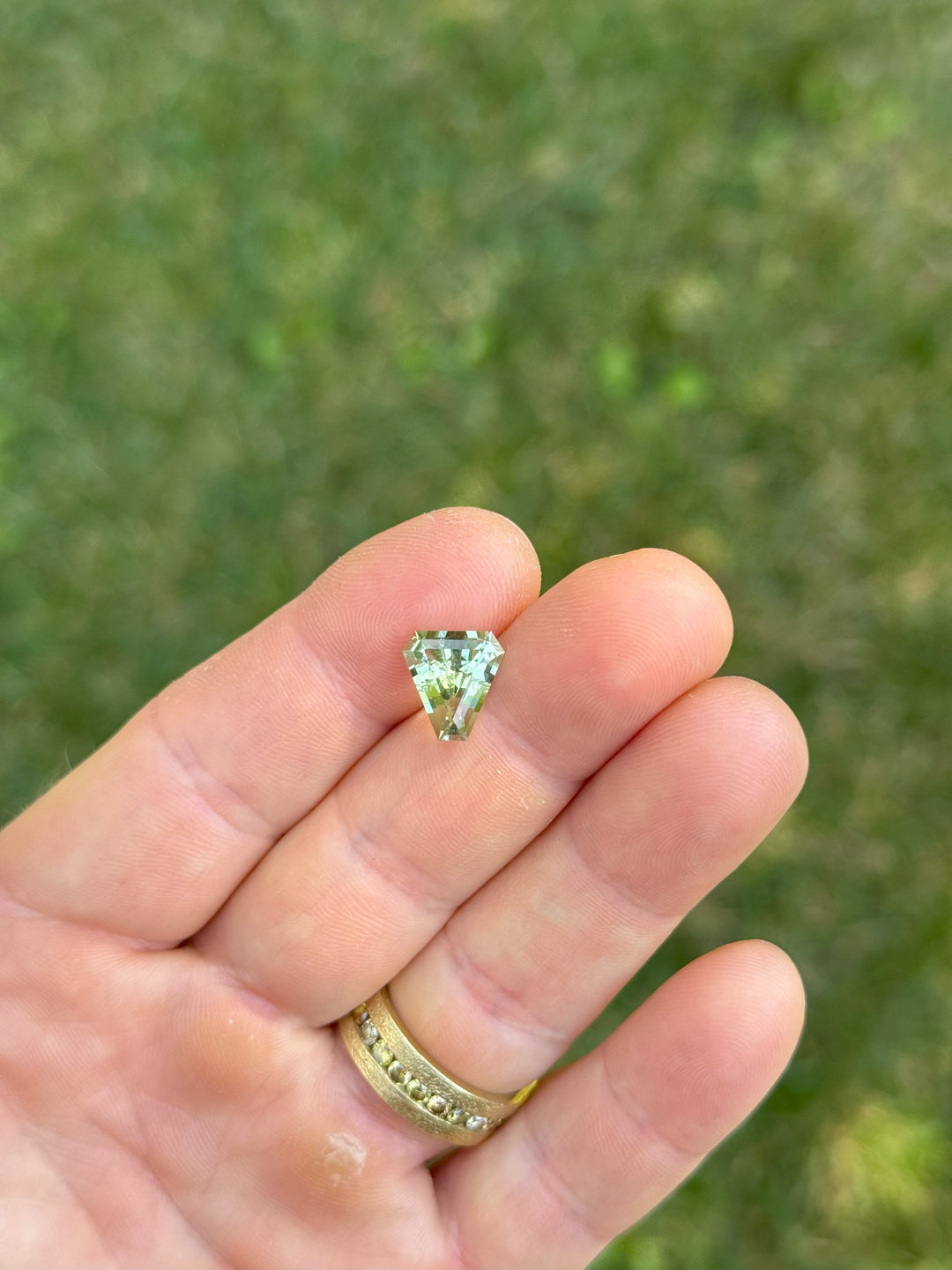 3.26CT mint green tourmaline shown on fingertip for scale, highlighting its geometric shield step cut and natural clarity, no-heat gemstone mined in Congo, Africa.
