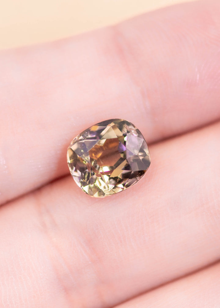 3.27 carat natural tanzanite displayed on a fingertip for scale, showcasing a purple-pink-peach color blend in a custom old mine cut, untreated gemstone sourced from Merelani Hills Tanzania
