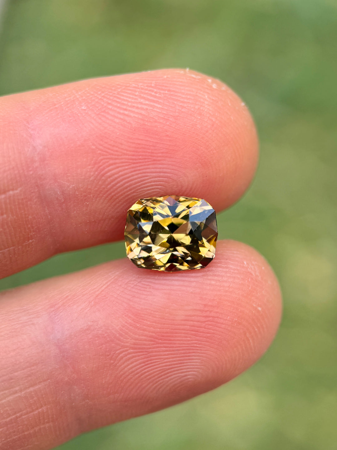 3.81 carat fancy Tanzanite balanced on fingertips for scale, highlighting its golden yellow and soft lavender reflections with intricate geometric cushion modified brilliant cut facets, natural and untreated from Merelani Hills, Arusha Region, Tanzania.