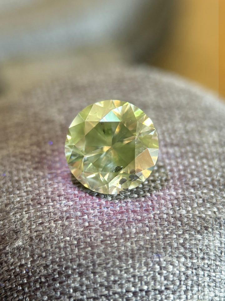 Natural 3.99 carat Fancy Dark Gray round brilliant diamond displayed on textured fabric surface, showing internal reflections and gray body color under mixed lighting.