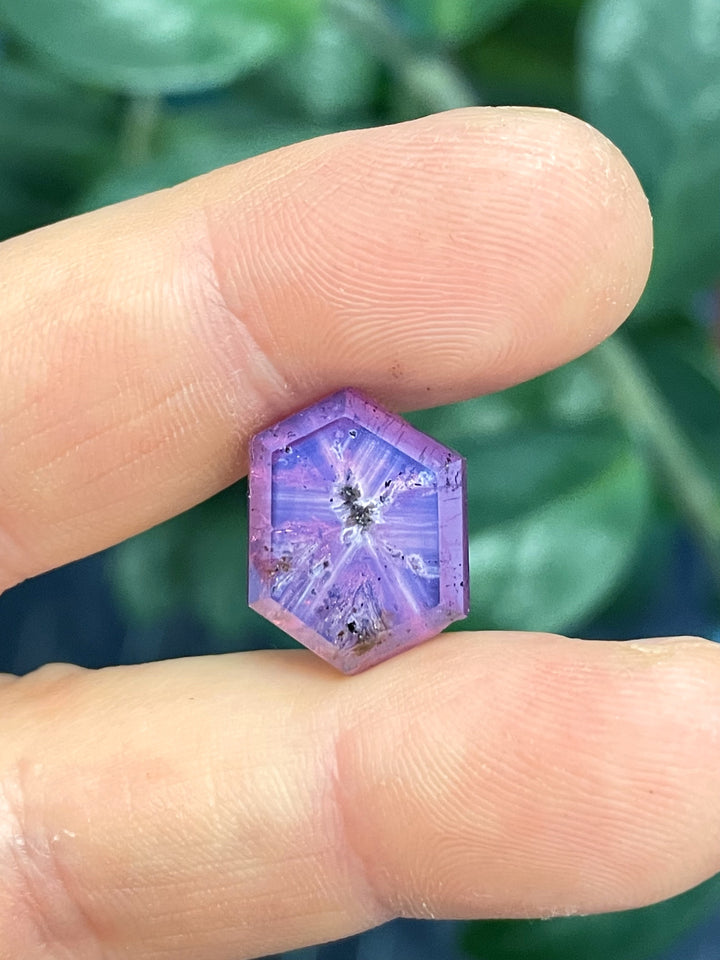 A stunning 19.62-carat sapphire from Afghanistan, displaying a vibrant mix of pink and purple hues in a hexagon portrait cut, held in precision fingers.