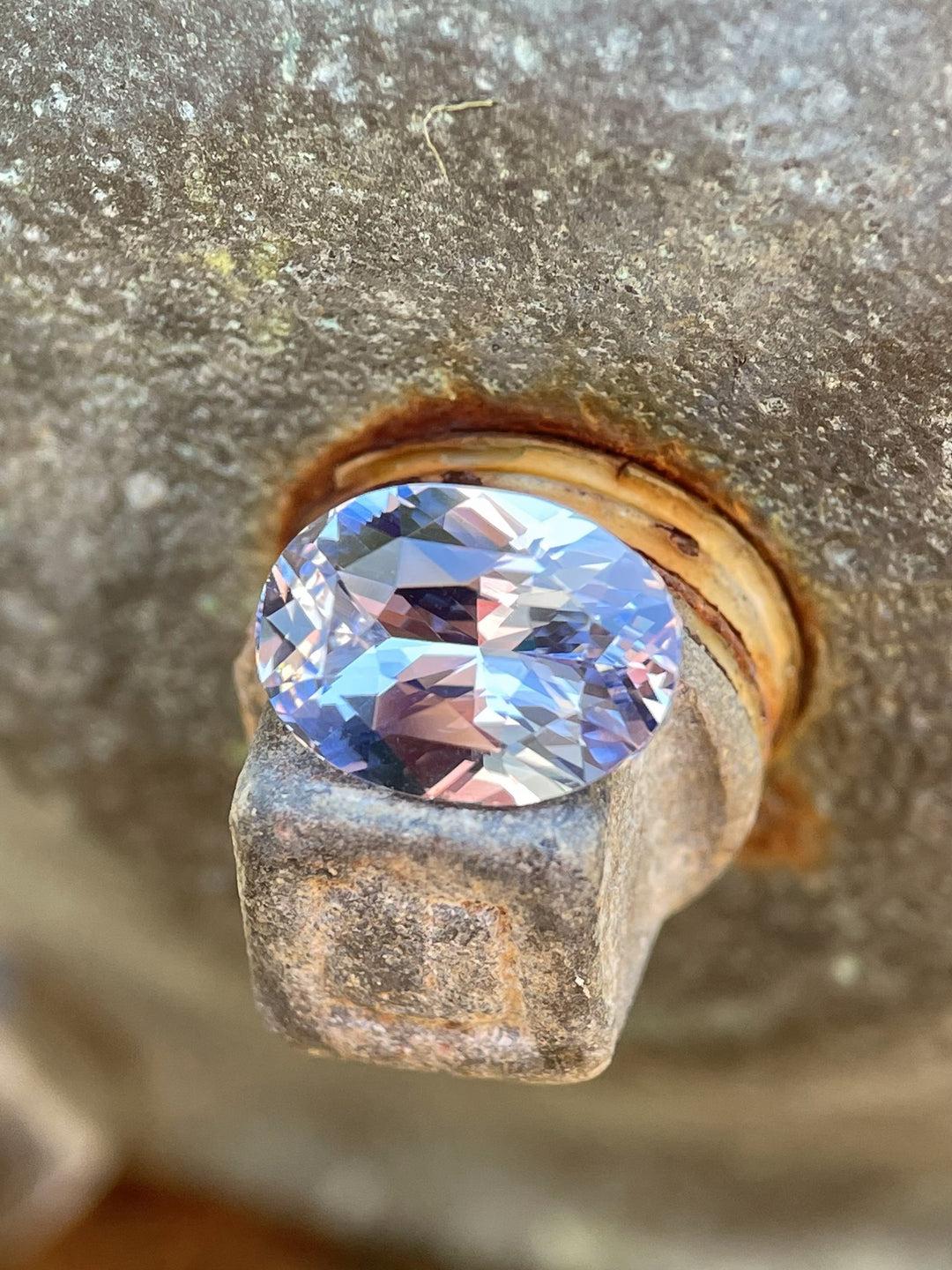 Close-up of a 3.03 carat untreated sapphire with a mix of lavender, pink, and purple set on a rustic metal background.