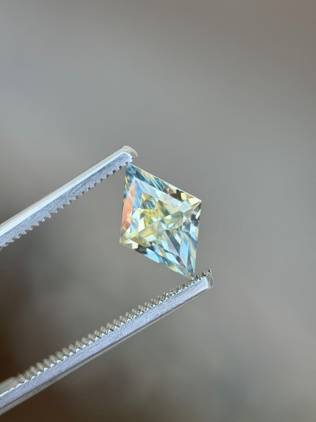 Precision-cut 3.07 carat parti sapphire from Madagascar held in gem tweezers, showcasing brilliant yellow and blue hues