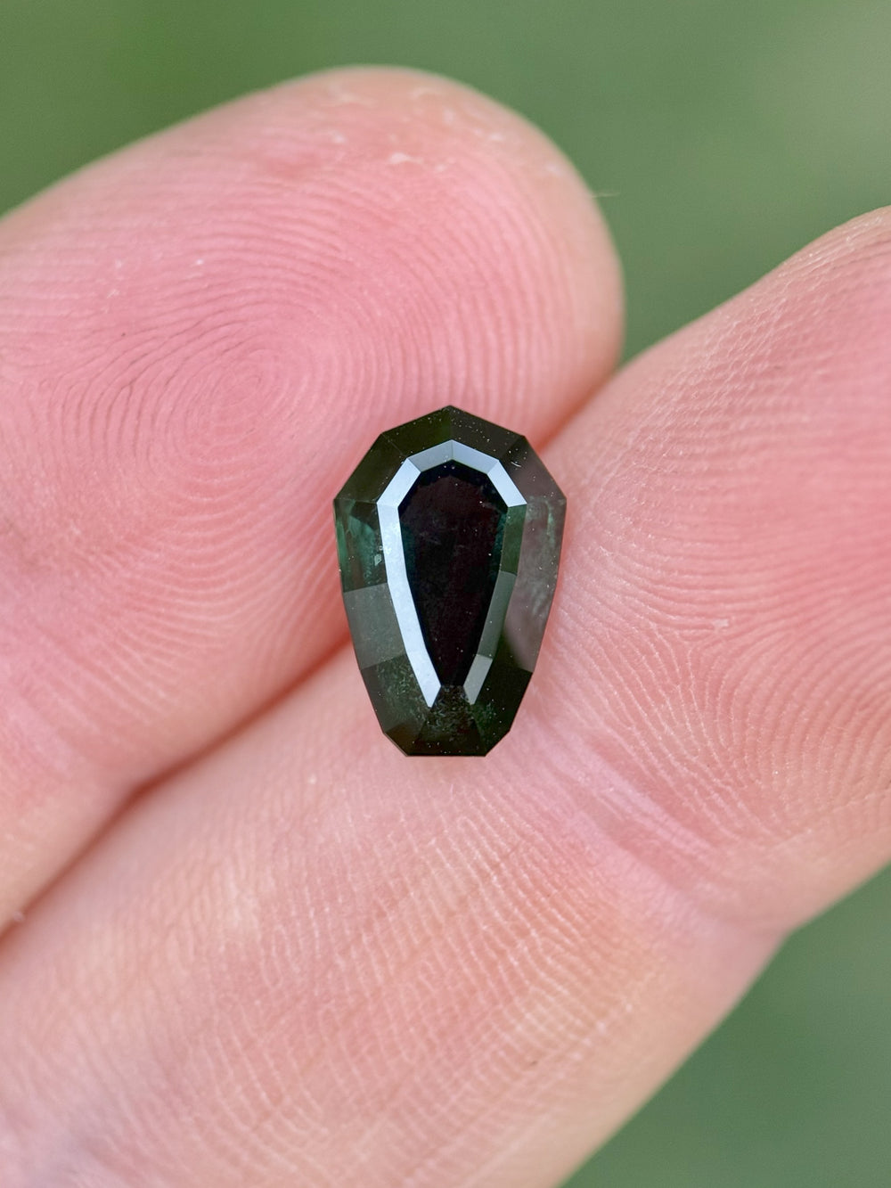 Close-up of untreated Nigerian sapphire, 3.07 carats, custom shield step cut with rich blue-green hues shown on a fingertip.