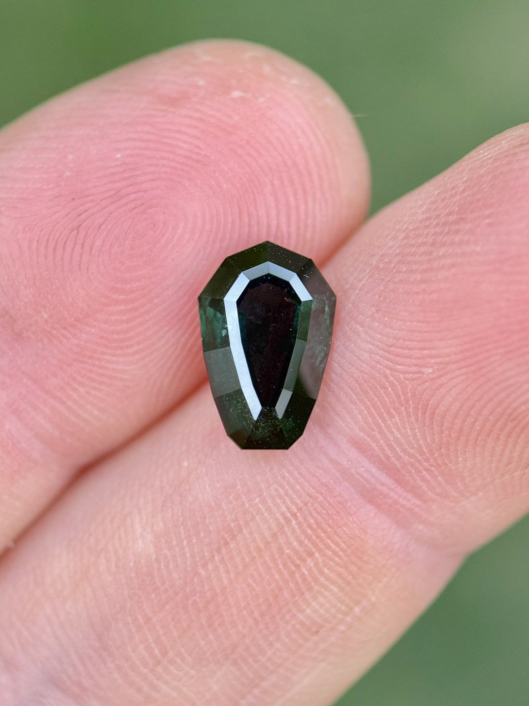 Close-up of untreated Nigerian sapphire, 3.07 carats, custom shield step cut with rich blue-green hues shown on a fingertip.