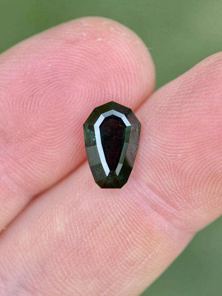 Close-up of untreated Nigerian sapphire, 3.07 carats, custom shield step cut with rich blue-green hues shown on a fingertip.