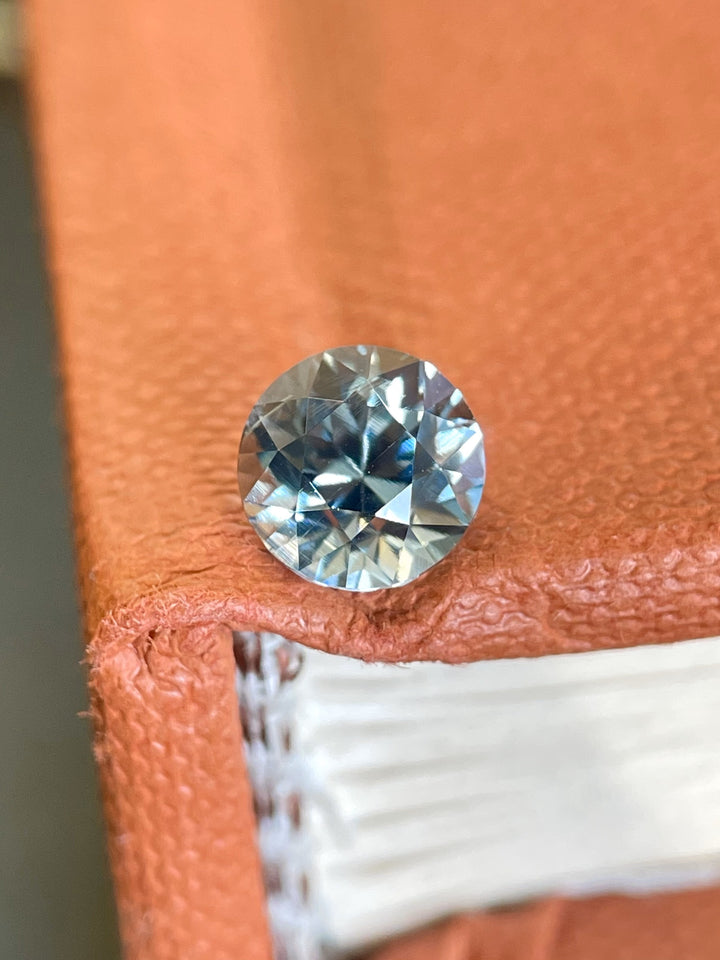 Close-up of a 2.04-carat round brilliant seafoam sapphire on the corner of a textured book, showing off its dazzling sparkle and color blend.