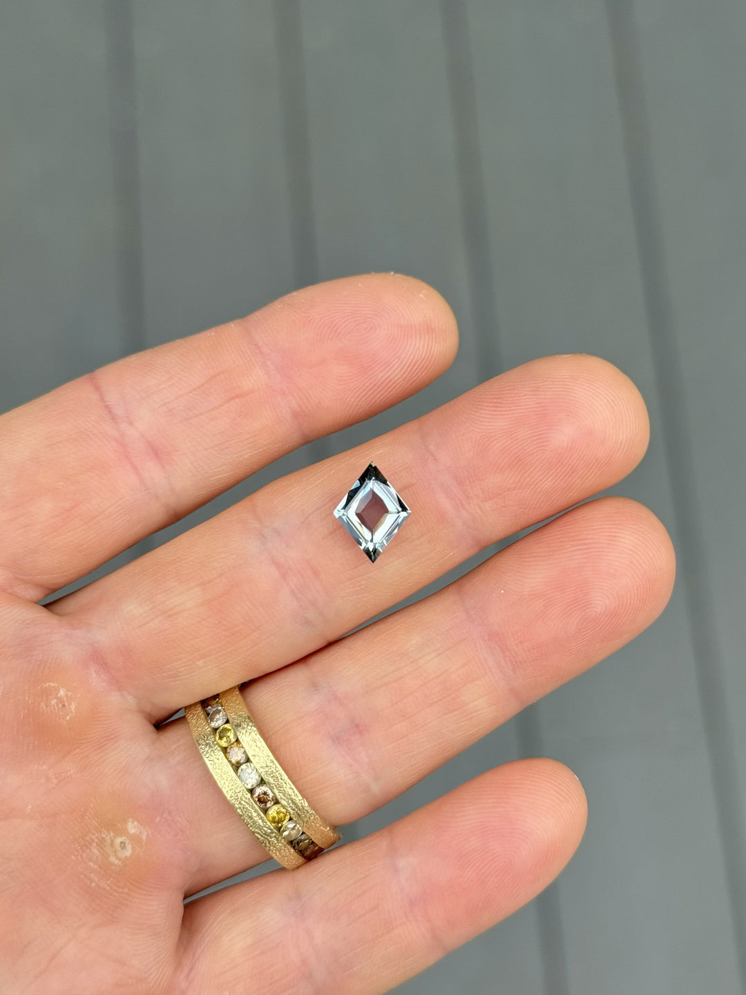 Custom antique-style lozenge kite cut sapphire displayed on hand, 2.68ct untreated gem with color shift from seafoam to bluish gray