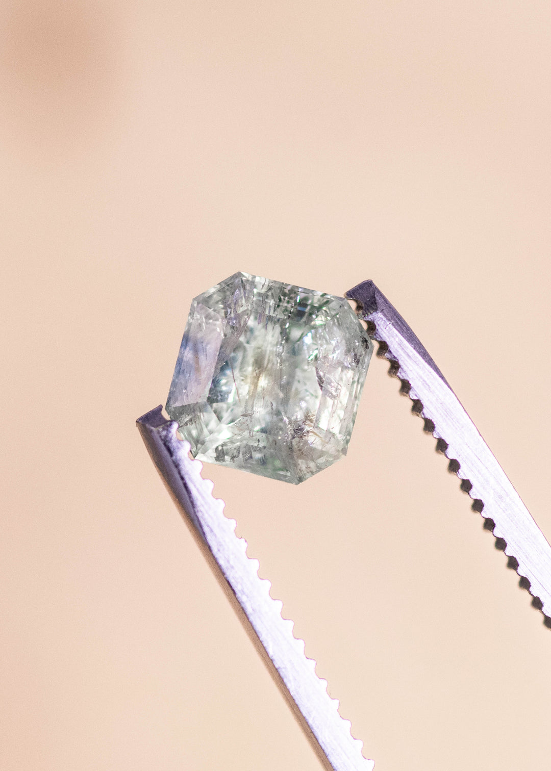 Seafoam teal Montana sapphire held in professional gem tweezers, showcasing a precision Asscher cut with sharp step facets, natural inclusions, and unheated clarity captured in close-up macro detail.