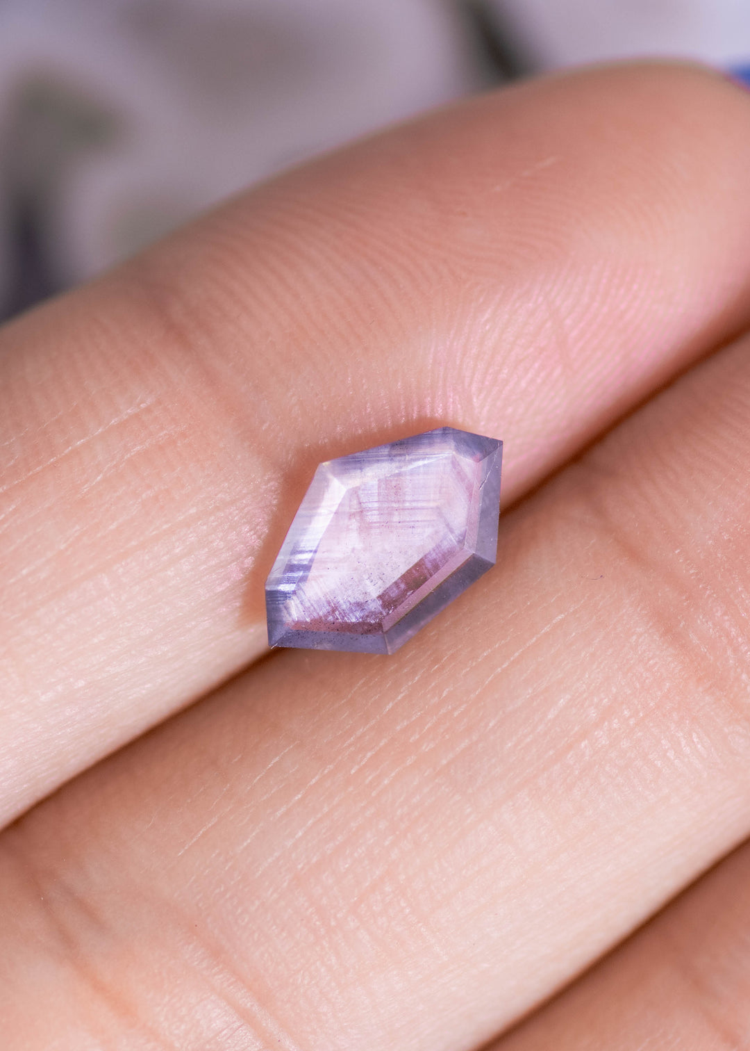 Hand-held macro photo of a 1.22ct untreated Sri Lanka sapphire with purple brown gray parti tones, showcasing thin portrait cut profile and precision faceting.