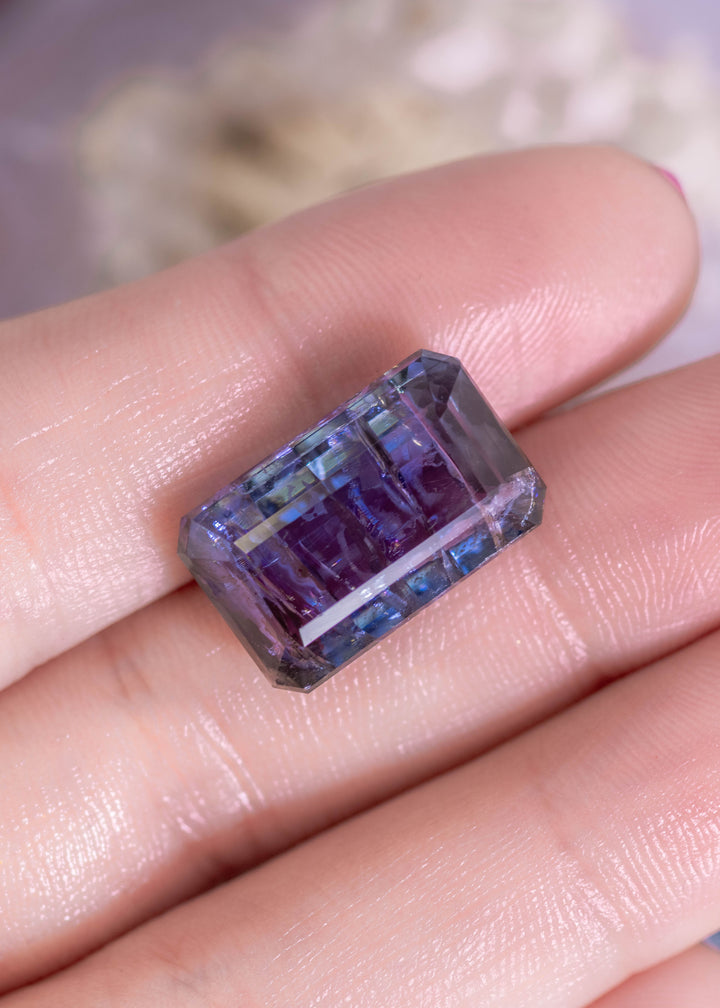 Large 18.04 carat Tanzanite resting on fingertips to show scale and proportions, featuring vivid teal, blue, and violet tones in a custom octagonal step cut