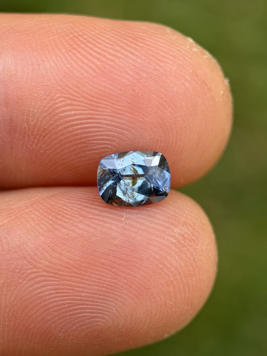 1.23CT teal blue to purple sapphire resting on fingertip, showcasing its color shift and cushion cut.