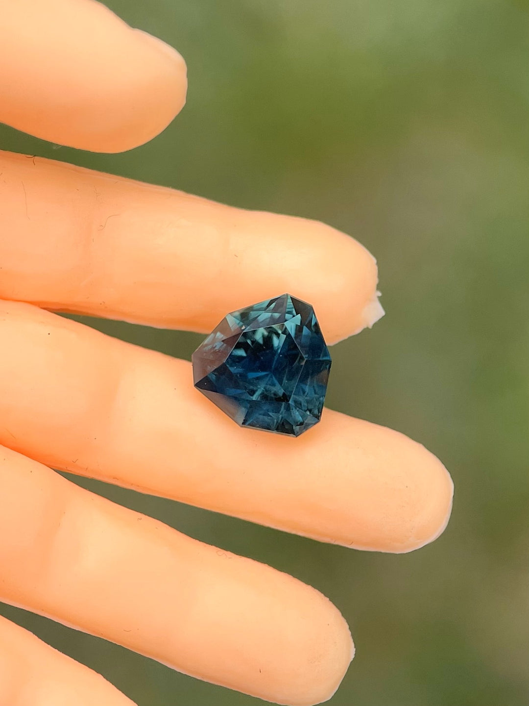 Close-up view of a 1.43-carat no-heat sapphire in a custom trillion cut. The gemstone shines in deep teal and blue-green shades, emphasizing its unique geometric design. Captured on a mannequin's finger, the gem’s vivid color and clarity stand out.