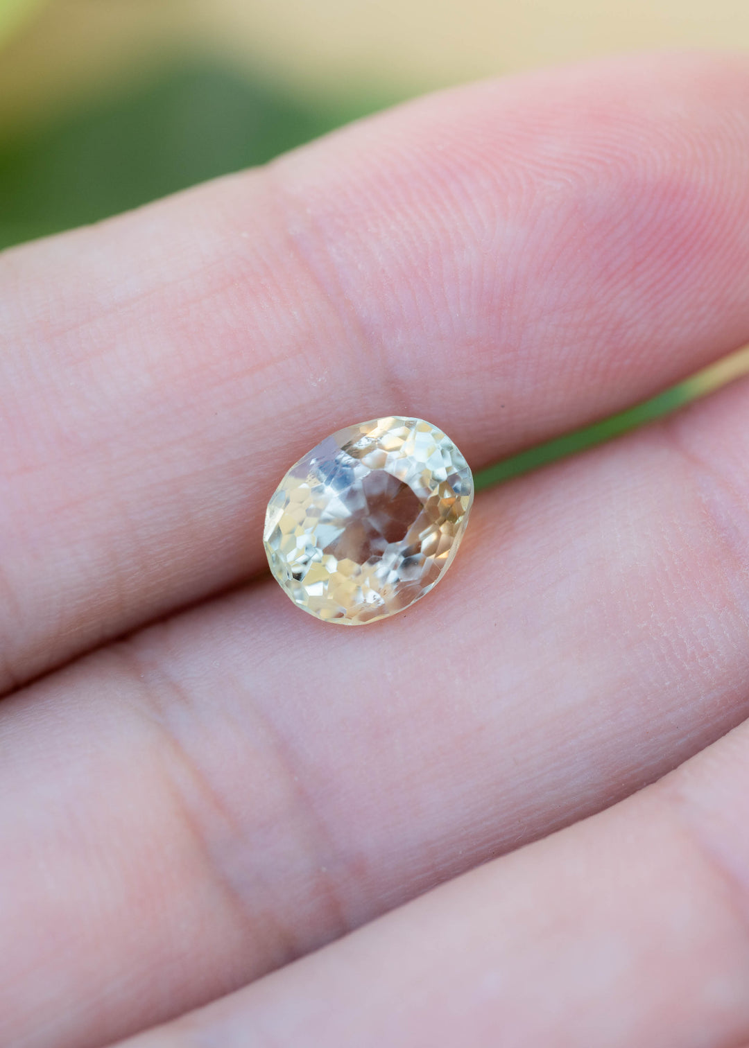 Vintage 2.34 carat yellow tourmaline resting on fingertips for scale, showing its pale butter yellow color, oval brilliant mix cut and softly organic vintage faceting.