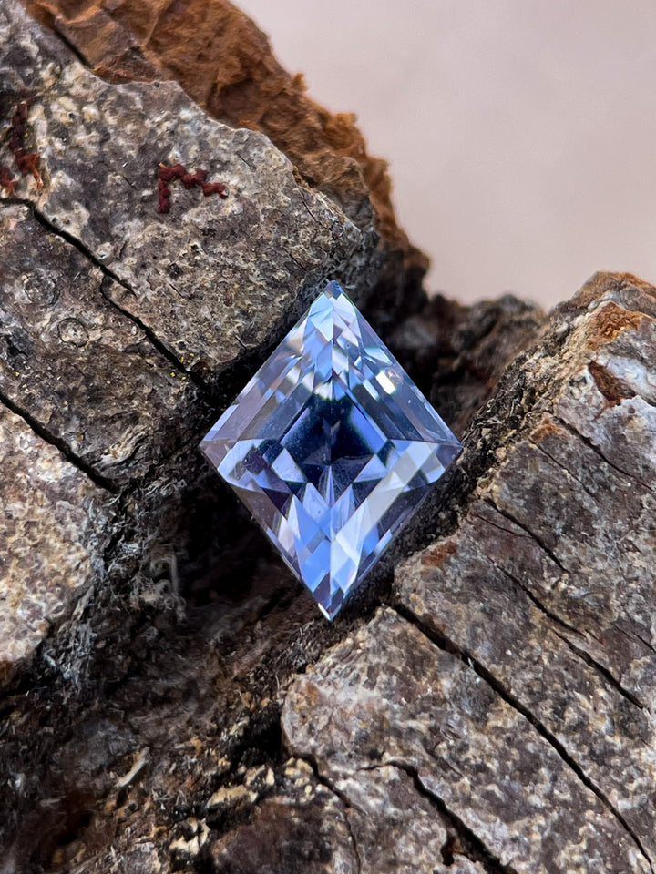 A 1.53-carat violet-blue sapphire with a kite step cut, featuring sharp geometric lines. Sri Lankan origin, displayed on a natural wood texture.